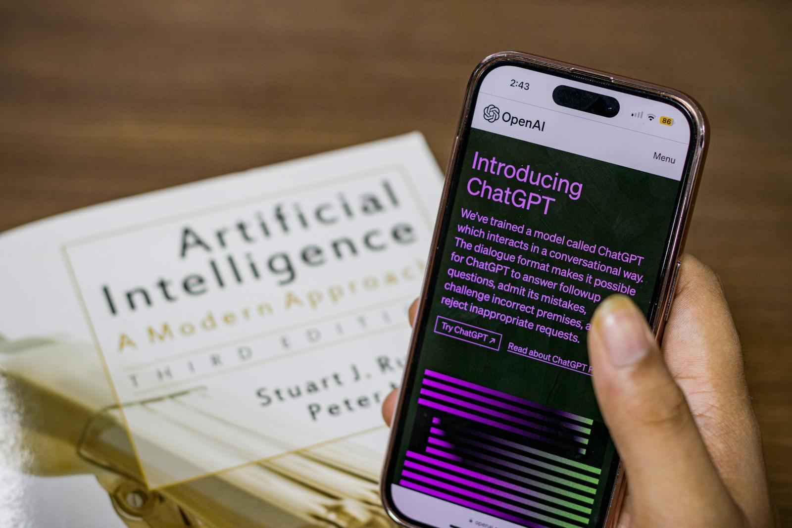 Eine Person hält ein Smartphone mit ChatGPT-Anzeige neben einem Buch über künstliche Intelligenz